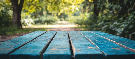 Poster - Tranquil blue wooden table in foreground surrounded by lush green trees and soft sunlight creating a peaceful garden atmosphere for relaxation