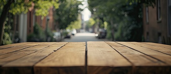 Leinwandbilder - Wooden table in foreground with intricate grain texture, blurred vibrant street scene featuring greenery and soft light in background