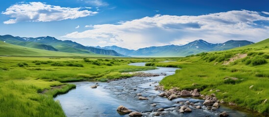 Poster - Serene landscape with a flowing river in the foreground, vibrant green fields in the midground, under a bright blue sky with fluffy white clouds.