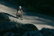 © Cavan Images - Cyclist on a gravel road winding through a dense forest with shadows.