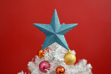 Wall Mural - Beautifully decorated Christmas tree topped with a sparkling blue star against a vibrant red background during the holiday season