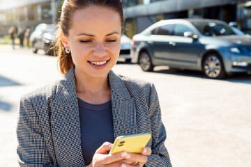 Wall Mural - Businesswoman using her smart phone while standing on city street.