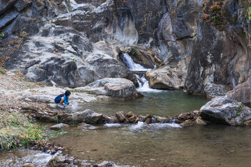 Wall Mural - asian child playing waterfall or kid girl sitting in natural water with rocks stones or young woman trekking camping on nature stream in summer and forest for holiday travel adventure at lan sang