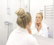 © lado2016 - woman looking in the mirror in the bathroom and taking care of her skin.
