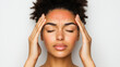 © Winter KD - young woman with curly hair is holding her head, expressing discomfort. Her eyes are closed, and her facial expression suggests she is experiencing headache or stress