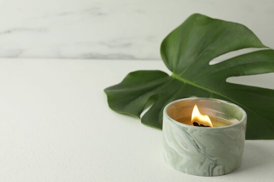 Wall Mural -  - burning soy wax candle and monstera leaf on light table, closeup. space for text