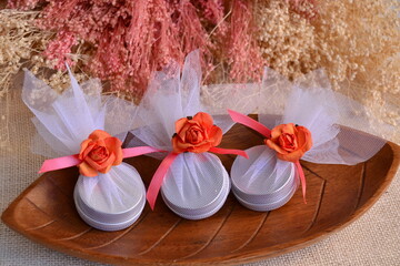 Wall Mural - Wedding favors wrapped round gift boxes, white orange pink silver color, lip balms guest souvenirs, ribbon bow flower, beautiful packaging presents for party event guest, wooden plate background