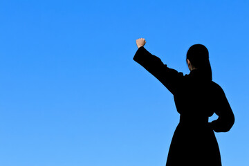 Wall Mural - A woman is standing in the sky with her arms raised, looking up at the blue sky