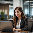 © Busy Man - A Hispanic female professional sitting at her desk and smiling slightly while focusing on her laptop screen.