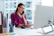© Home-stock - Female manager talking on cellphone and taking notes, sitting at her desk in office, working at table with computer answers calls