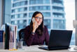 © Home-stock - Happy business lady, broker or manager, sitting at workplace in modern office, working with laptop and talking to client or employees on smartphone
