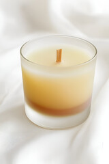 Canvas Print - Acylindrical, amber-hued candle with a light wood wick sits on a white fabric background.