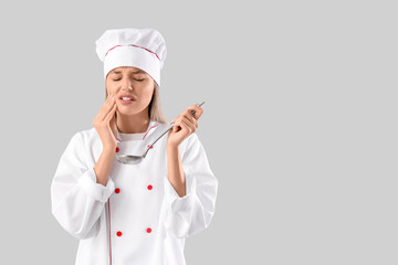 Wall Mural - Young female chef with ladle suffering from tooth ache on grey background