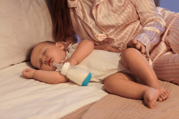 Canvas Print - Cute little baby with bottle of milk and mother sleeping on bed at night, closeup