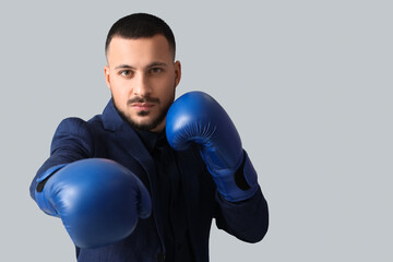 Wall Mural - Young businessman with boxing gloves on light background. Knockout concept