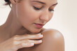 © Buyanskyy Production - Close-up of a woman with smooth, glowing skin gently touching her shoulder with a serene expression. The soft beige background complements her natural beauty and highlights her skincare routine.