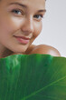 © Buyanskyy Production - Close-up of a young Caucasian woman with glowing skin holding a dewy green tropical leaf, symbolizing natural beauty and skincare. Perfect for eco-friendly and organic product promotions.