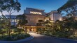 © PB Studio - A modern hospital building with a large illuminated hospital sign above the entrance, surrounded by trees and well-maintained landscaping.