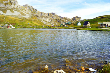 An idyllic rural landscape from Montenegro: a view of a lake in the mountains, houses with gabled roofs located on its shores and a flock of sheep grazing on a hillside. Kapetanovo jezero near Niksic.