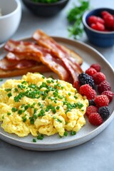 Wall Mural - A plate of fluffy scrambled eggs garnished with chives, served with crispy bacon strips, toast, and a small bowl of mixed berries.