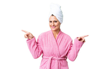 Canvas Print - Middle age caucasian woman in a bathrobe over isolated background pointing finger to the laterals and happy