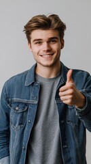 Poster - Young man in stylish denim jacket gives a thumbs up in minimalist setting with neutral background