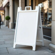 © RizzDesign - A blank white A-frame sidewalk sign stands on a city sidewalk. Perfect for advertising or announcements.