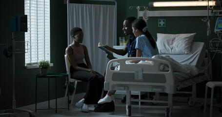 Wall Mural - African father and child sit on a hospital bed reading a book together. A mother sits with her child, and the family spends time together while the child is recovering from a serious illness.