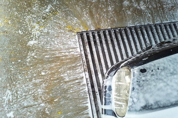 Soap sud waste flows to floor drain grid in car washing garage, close-up.