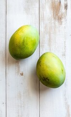 Wall Mural - Two green mangoes lying on a light wooden table, top view, close-up, stock photo.