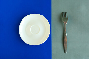 Empty plate and fork on blue and black background. Copy space for the text. Minimal concept