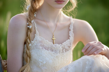 Wall Mural - A delicate portrait of a woman wearing a lace dress, a gold cross necklace, and a braided hairstyle adorned with flowers