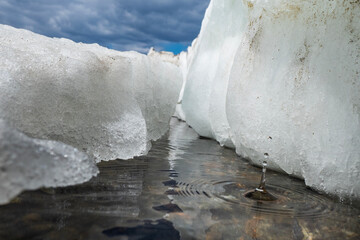 Fototapete - Melting blocks of ice lie on the shore of the frozen Sea of Okhotsk. A close-up photo shows how ice melts and flows into the water as drops.