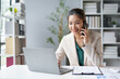 © Crystal - Asian businesswoman talking on phone and working on laptop in office