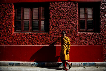 An indian man wearing an indian traditional bengali red dhoti and orange kurta posing outdoor fr a shoot in the streets of kolkata