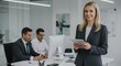 © Anomal - Woman smiling while holding tablet with man working at computer in modern office, emphasizing professional business environment