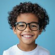 © bersch28 - A young boy with curly hair and glasses is seen smiling radiantly in front of a bright blue background, representing happiness, youthfulness, and positivity.