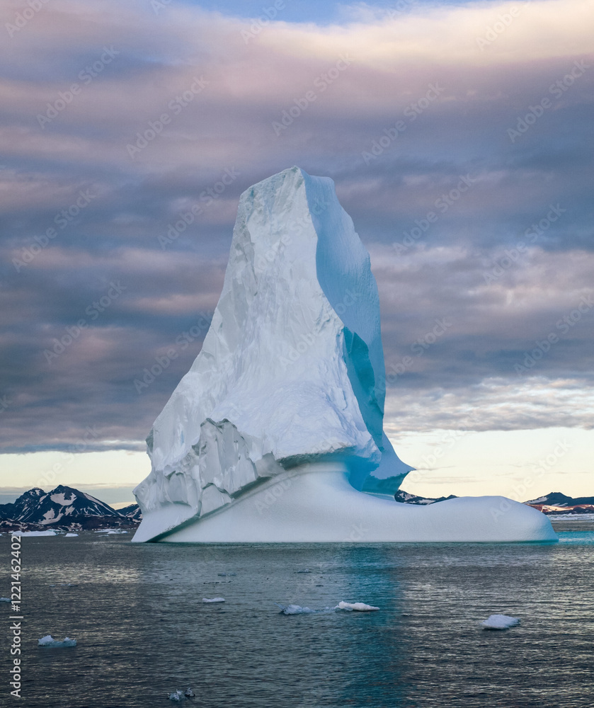 Iceberg in Greenland. Colorful huge Iceberg building. Large ice block floating in the ocean. The sky is cloudy and the sun is setting
