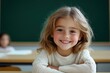 © Y_Malashkevych - A cheerful girl around seven years old smiles warmly while sitting at her desk in a clean school environment. With a green chalkboard behind her she exudes happiness and enthusiasm for learning