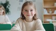 © Y_Malashkevych - A cheerful White European girl around eight years old is seated at a green desk grinning widely while looking straight at the camera
