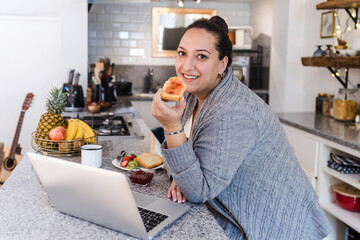 Wall Mural - young latin woman overweight using laptop while having breakfast at home kitchen in Mexico Latin America, hispanic plus size female	
