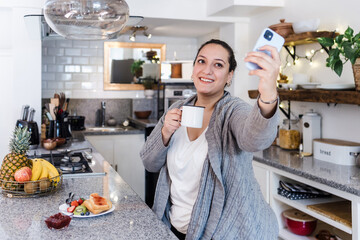 Wall Mural - young latin woman plus size taking a photo selfie with mobile phone in kitchen at home in Mexico Latin America, hispanic overweight female 	