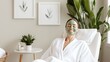 © Y_Malashkevych - A joyful woman in her 30s relaxes in a minimalist spa setting wearing a white robe and a green clay facial mask. Natural light fills the room enhancing her cheerful smile and calm atmosphere