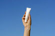 © Daryna  - Female hand with smear sample holds white blank tube of natural face or eye cream on blue sky background. Concept of aesthetics and beauty care products. Mockup for your design
