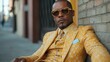 © aicandy - Portrait of a confident man in a distinctive, vibrant yellow suit with stylish sunglasses, sitting thoughtfully against an urban brick wall backdrop on a city street.