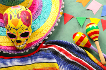 Wall Mural - Mexican maracas with painted skull, sombrero hat, serape and flags on green background, closeup