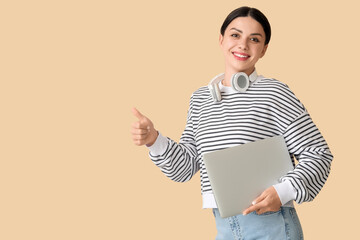 Female programmer with laptop showing thumb-up on beige background