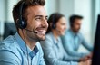 © Maryna - Friendly call center employee smiles warmly talking on headset. Pro young male operator wearing headset, light blue shirt in modern office. Happy support agent communicates with client in pleasant