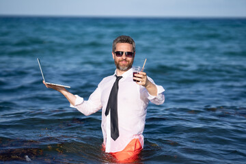 Wall Mural - Fun business lifestyle. Freelance work, distance online work, e-working. Summer business. Business man in shirt remote working on laptop in sea water. Business man working online.