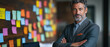 © CreativeIMGIdeas - Confident Businessman: Portrait of a mature, successful businessman with salt and pepper hair, standing confidently with his arms crossed in front of a wall covered in colorful sticky notes.